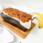 finished banana bread in baking tin beside two bananas