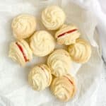 gluten free whipped shortbread cookies with buttercream and jam filling on a white plate