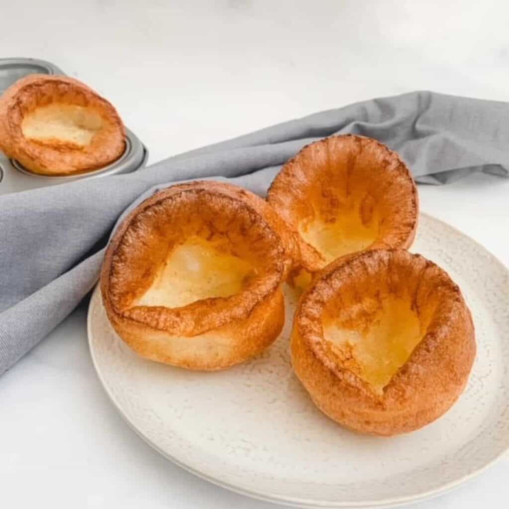 3 yorkshire puddings on a white place with a grey napkin in the background