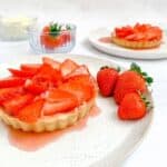 gluten free strawberry tart on a white plate with loose strawberries beside it