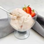 strawberry ice cream in a glass bowl with a strawberry placed on the side