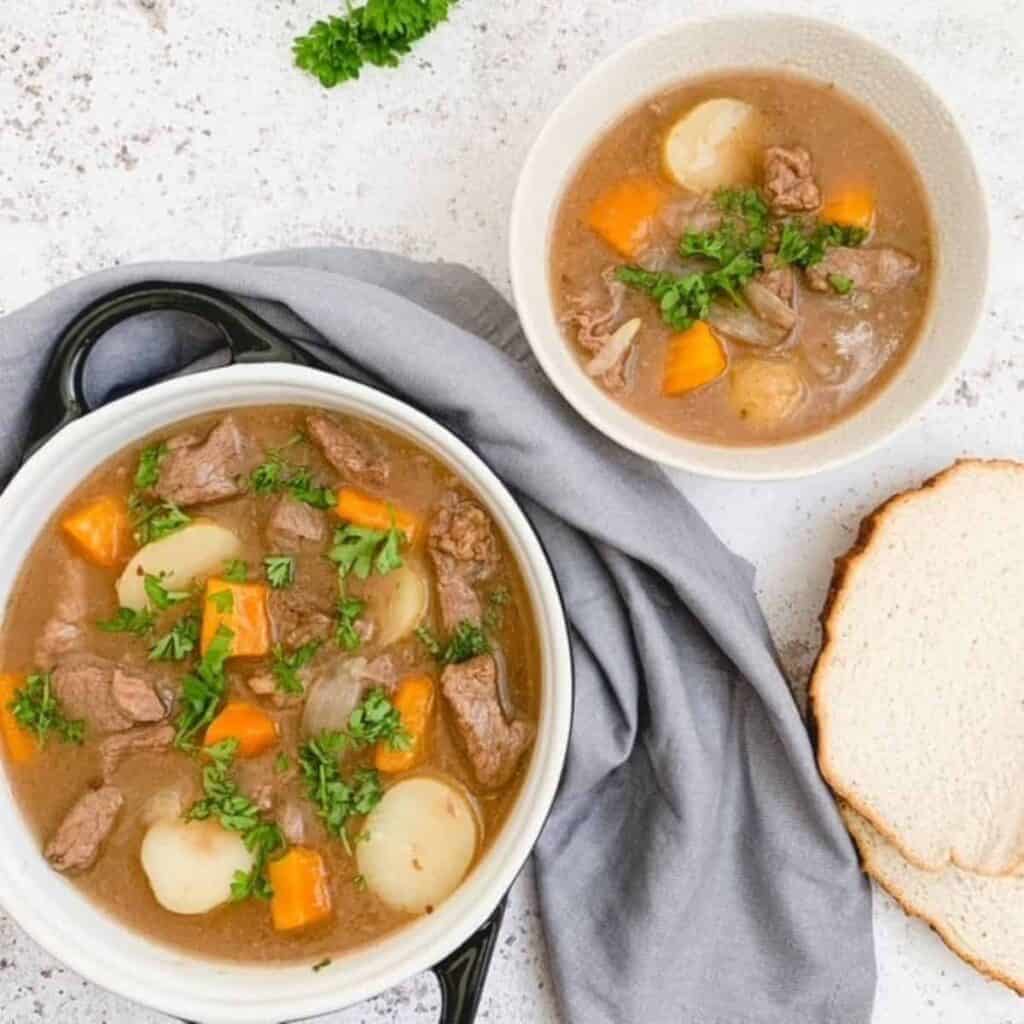 Gluten free beef stew in a large serving dish with a small bowl of stew and two slices of bread