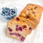 Gluten free blueberry banana bread with two pieces sliced with a small bowl of blueberries