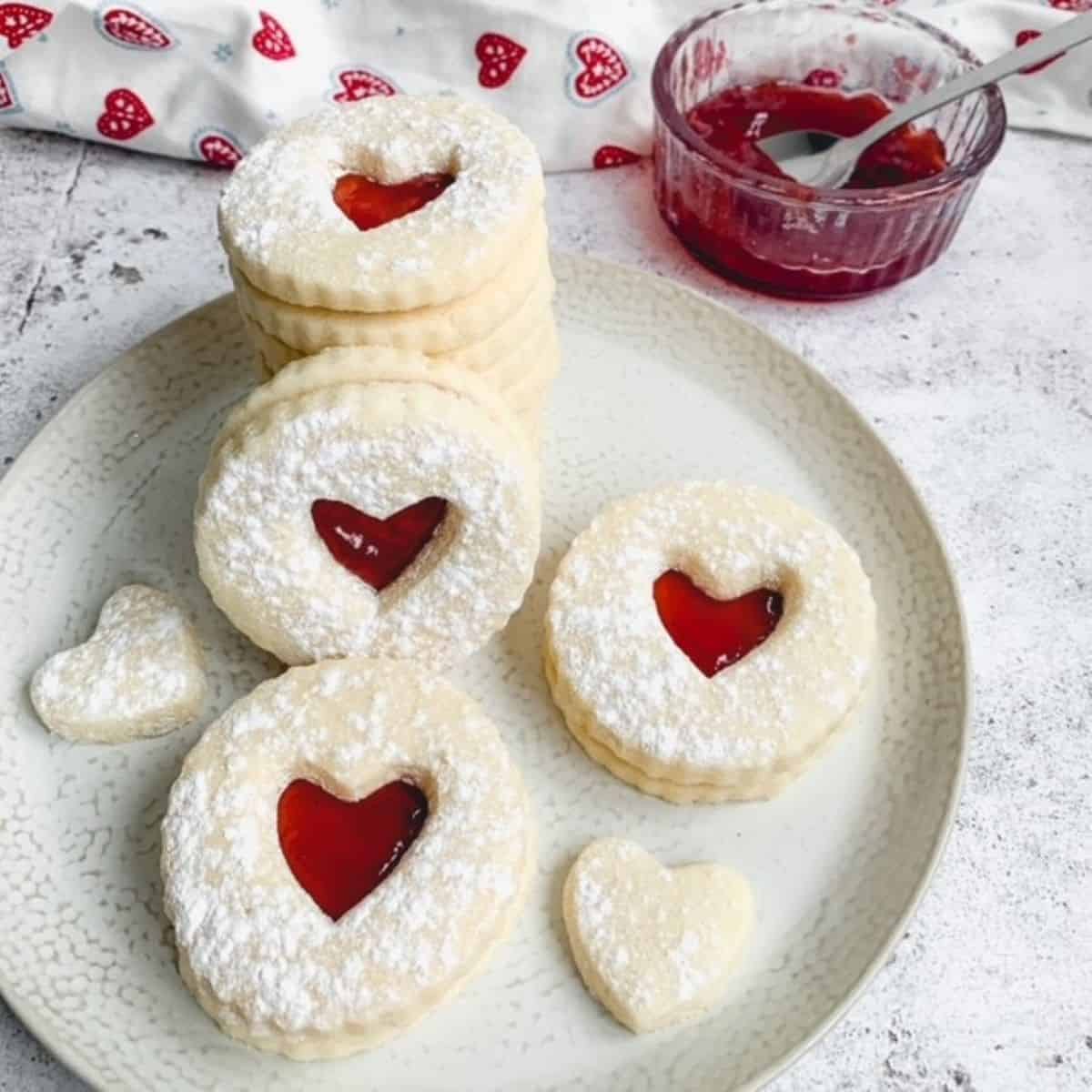 jammy dodger biscuits stacked on a white plate with a small glass bowl of jam in the background