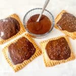 four gluten free chocolate pop tarts beside a small bowl of chocolate icing