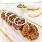 chapli kababs on a wooden serving board with pitta bread and salad in the background