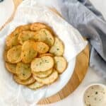 cottage fries in a white bowl on top if a wooden chopping board beside a small pot of garlic dip