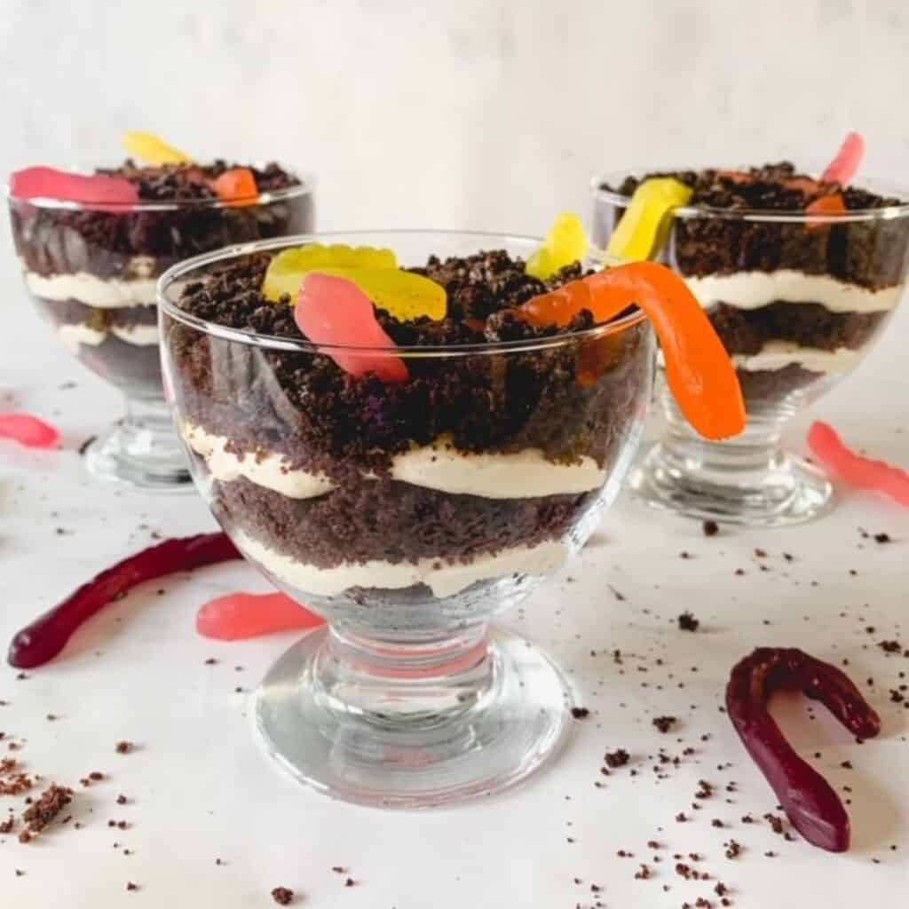 3 dessert glass bowls with gluten free dirt pudding surrounded by gummy worms