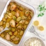 lemon chicken tray bake on a white worktop with a side of rice and sliced lemon