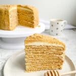 slice of medovik cake on a white plate with the full layer cake in the background