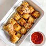 gluten free sausage rolls in a white rectangle serving dish with a small bowl of tomato sauce on the side