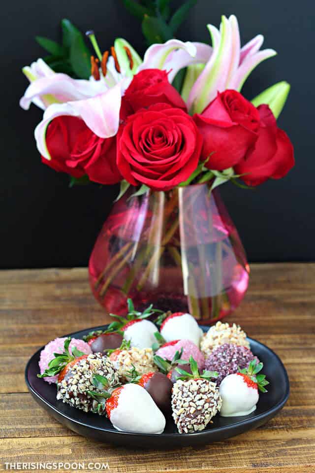 strawberry covered chocolates with a vase of flowers behind