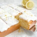 a slice of gluten free lemonade cake being removed from the cake with a sliced lemon in the background.