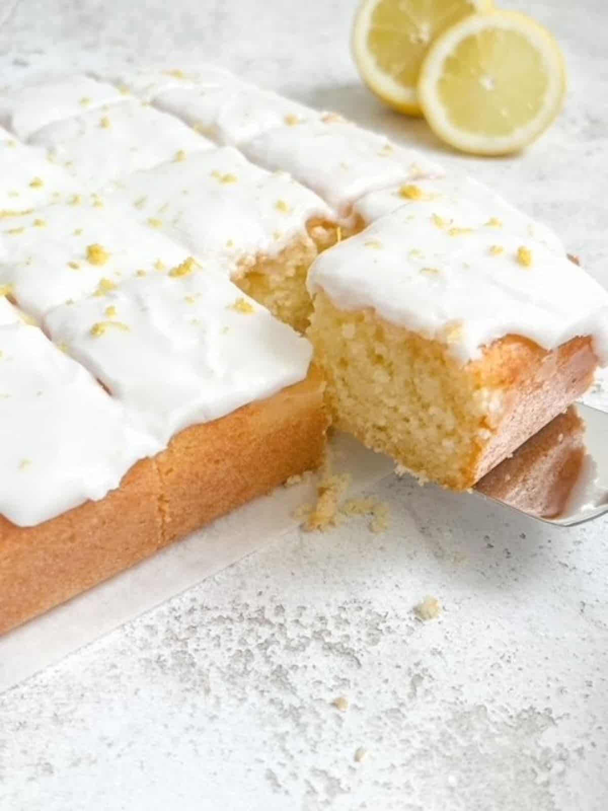 a slice of gluten free lemonade cake being removed from the cake with a sliced lemon in the background.