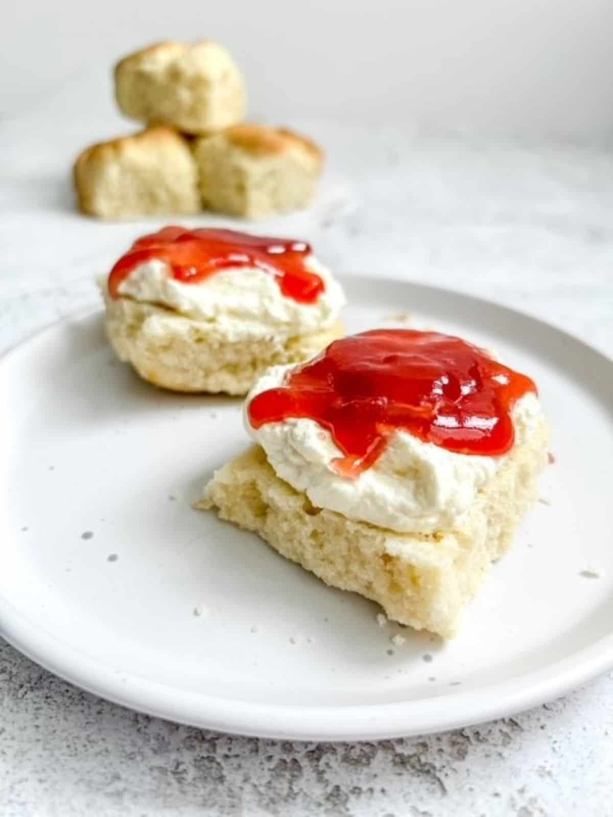 gluten free lemonade scones topped with whipped cream and jam on a white plate.