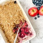white rectangle dish with apple and blueberry crumble with a serving spoon.
