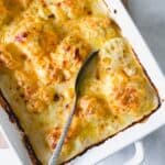 gluten free cauliflower cheese in a white dish with a spoon.