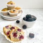 gluten free blackberry muffins stacked on a white plate with one muffin sliced in half.