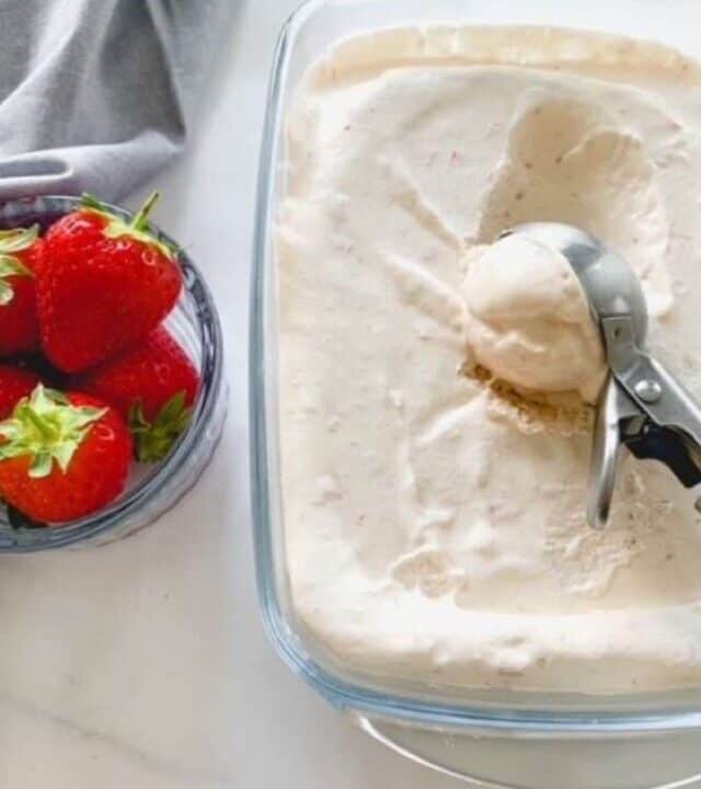 strawberry ice cream with an ice cream scoop and a small dish with strawberries.