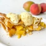 A slice of peach mango pie on a white plate topped with a scoop of vanilla ice cream.