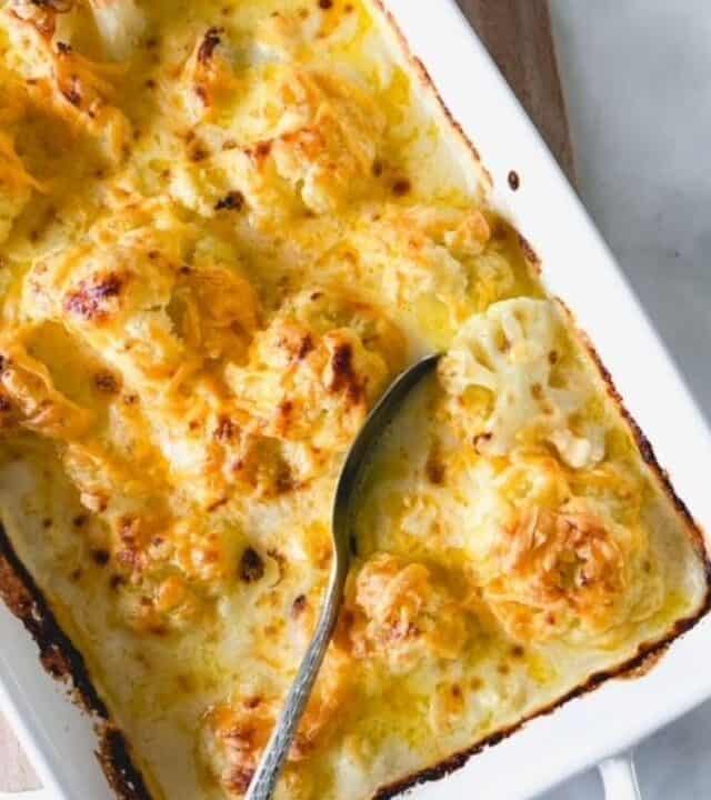 cauliflower cheese in a white baking dish with a spoon.