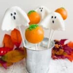 Ghost and pumpkin cake pops in a silver tin surrounded by autumn leaves.