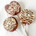 Three chocolate covered apple slices decorated in a halloween theme on a white background.