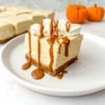 A slice of no bake pumpkin cheesecake bars with cream topping and drizzled in caramel sauce on a white plate.