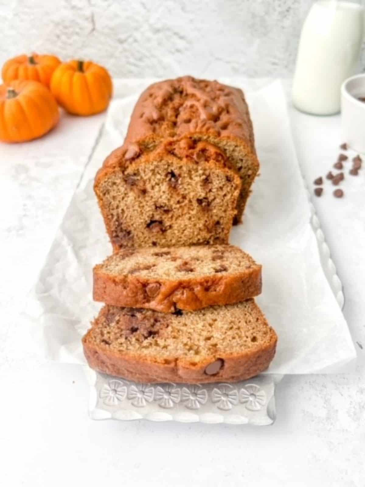 Gluten free chocolate chip pumpkin bread sliced on a white surface with mini pumpkins in the background.