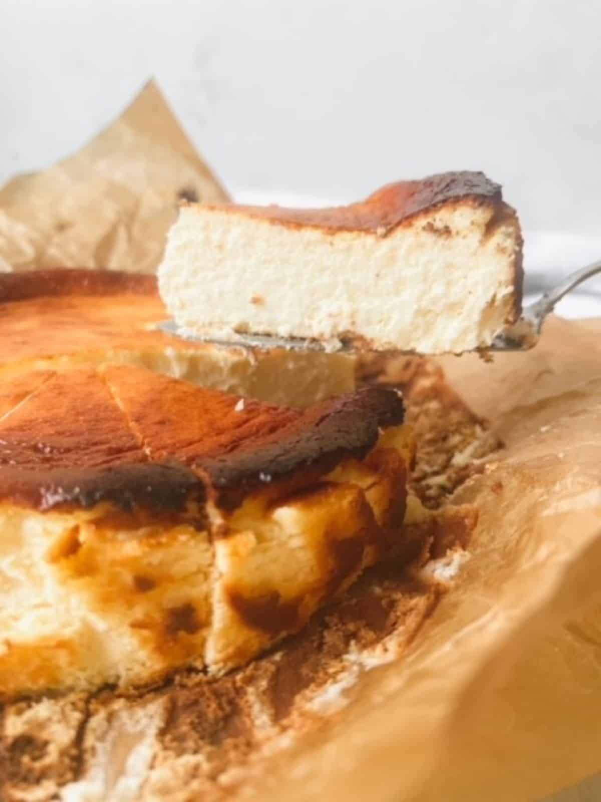 Basque cheesecake on brown parchment paper with a slice being lifted out.
