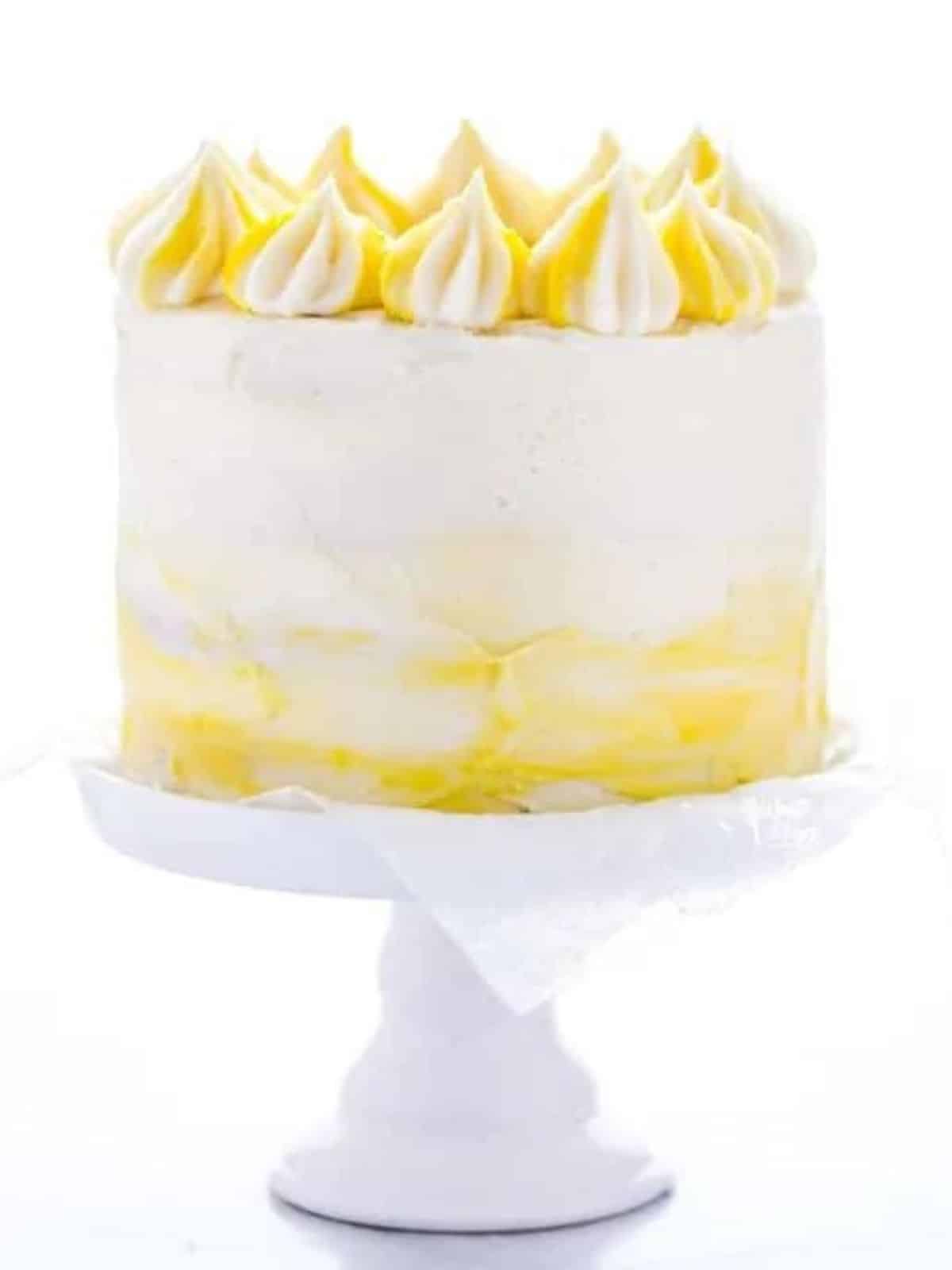 Lemon layer cake with mixture of white and yellow buttercream on a white cake stand.