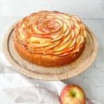 Gluten free apple cake on a wooden cake stand on a white background.