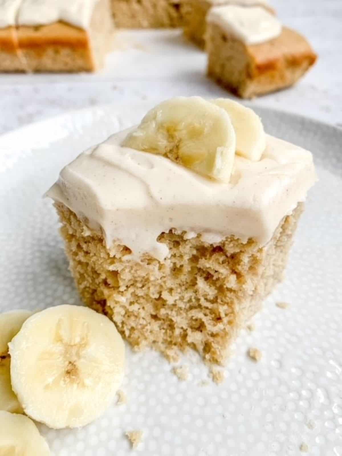 A slice of banana sheet cake topped with buttercream and fresh banana slices.