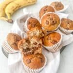 Gluten free banana muffins stacked together on top of a napkin with bananas in the background.