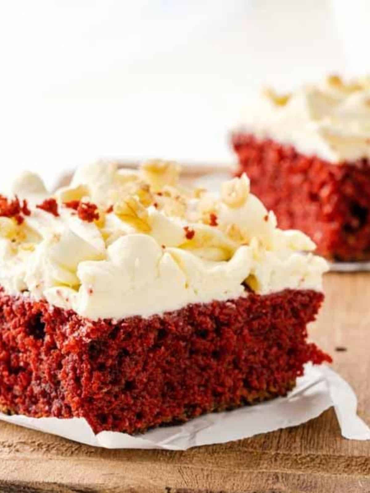 A slice of red velvet cake with cream frosting on a wooden board.
