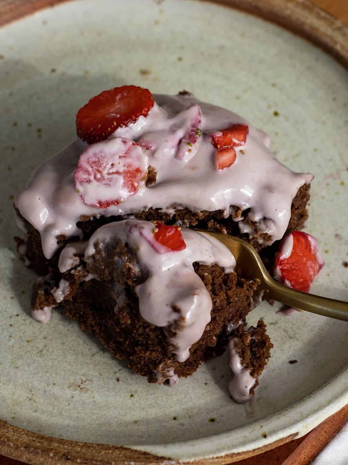 A slice of chocolate sheet cake with strawberry frosting on a grey plate with a fork.
