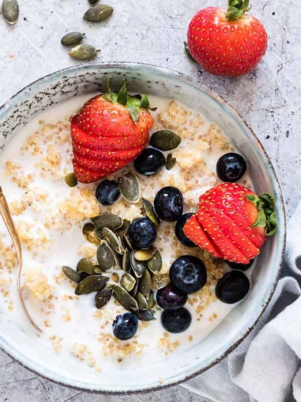 Quinoa porridge in a bowl topped with sliced strawberries and blueberries with a spoon.