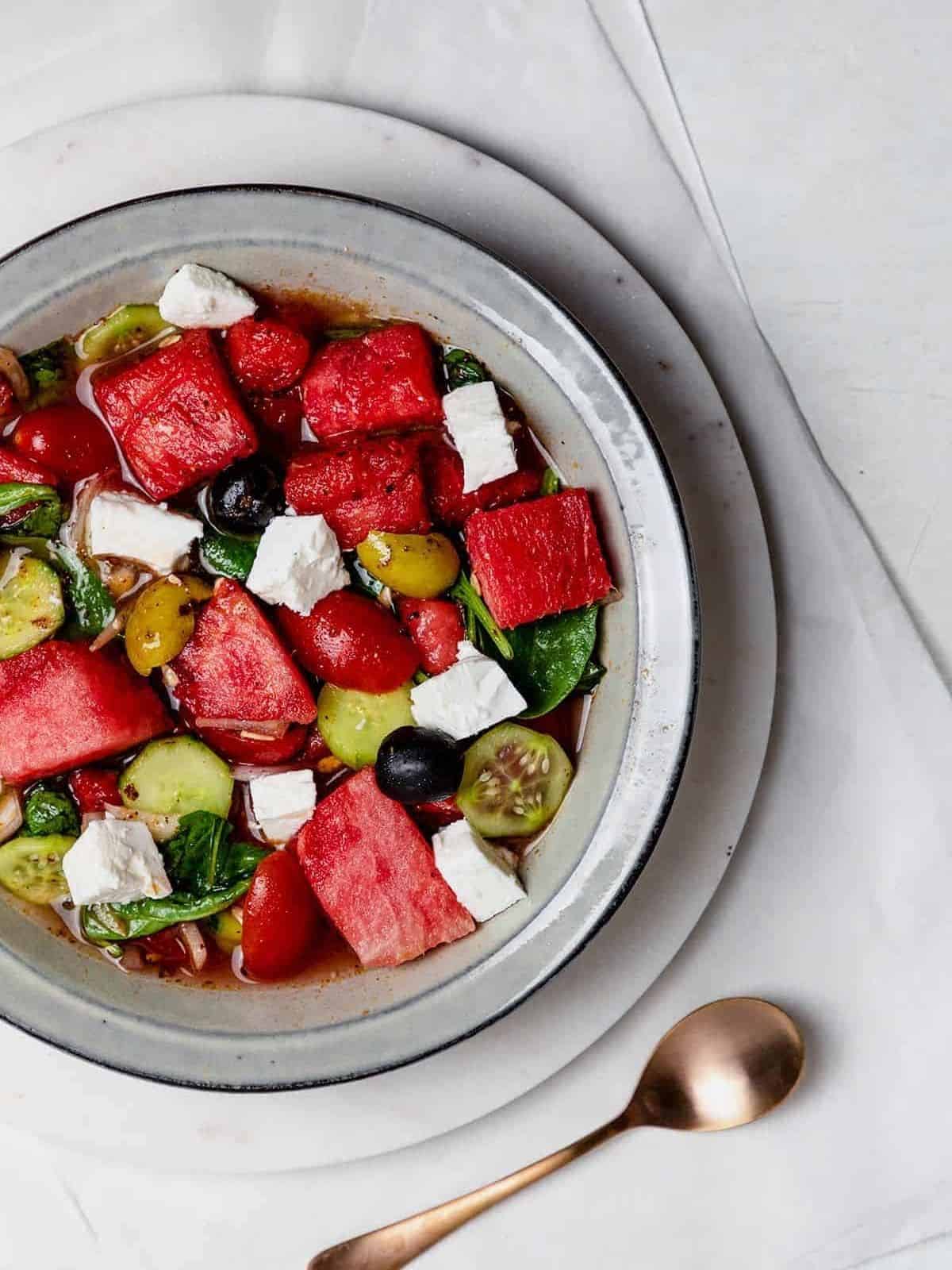 Watermelon and goat cheese salad in a bowl with a small spoon on the side.