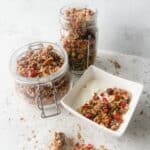 Gluten free granola in a small white bowl with greek yoghurt with two mason jars of granola behind.
