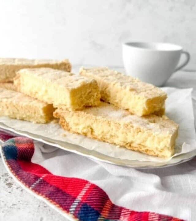 Gluten free shortbread stacked together on a silver serving plate on top of a tartan napkin.