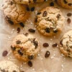 Gluten free oatmeal cookies with raisins stacked together on top of brown parchment paper.