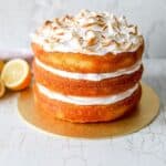 Lemon meringue cake on a white surface with sliced lemons on the side.