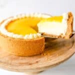 Lemon curd cheesecake with a slice being removed on a wooden cake stand.