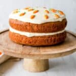 Gluten free carrot layer cake on a wooden cake stand with a white background.