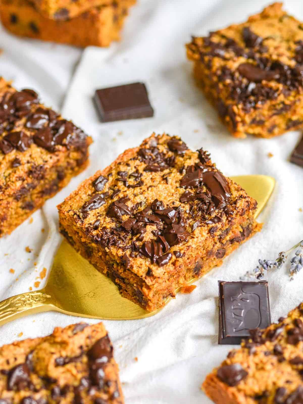 Gluten free pumpkin blondie squares on a white background with a gold cake server.
