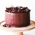 Gluten free dark chocolate cake on a wooden cake stand with a white background.