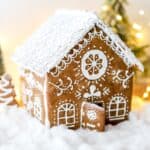 A gluten free gingerbread house dusted with powdered sugar on a white background.