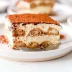 Close up of a slice of gluten free tiramisu on a white plate with a fork.