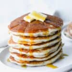 A stack of gluten free buttermilk pancakes topped with butter and syrup.