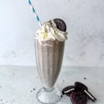 Tall glass filled with cookies and cream milkshake topped with whipped cream and an Oreo cookie.